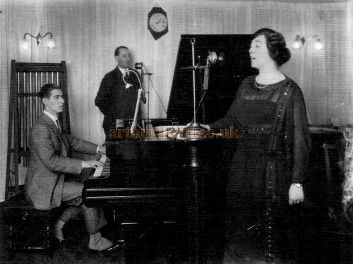 Miss Olive Sturgess and Mr. John Huntingdon singing a duet in the Marconi House studio in 1922. Mr. R. Stanton Jefferies, A.R.C.M. is the accompanist. In the background are the chimes which were then used to give the time signals. - Courtesy John A. Strubbe F.R.I.B.A.